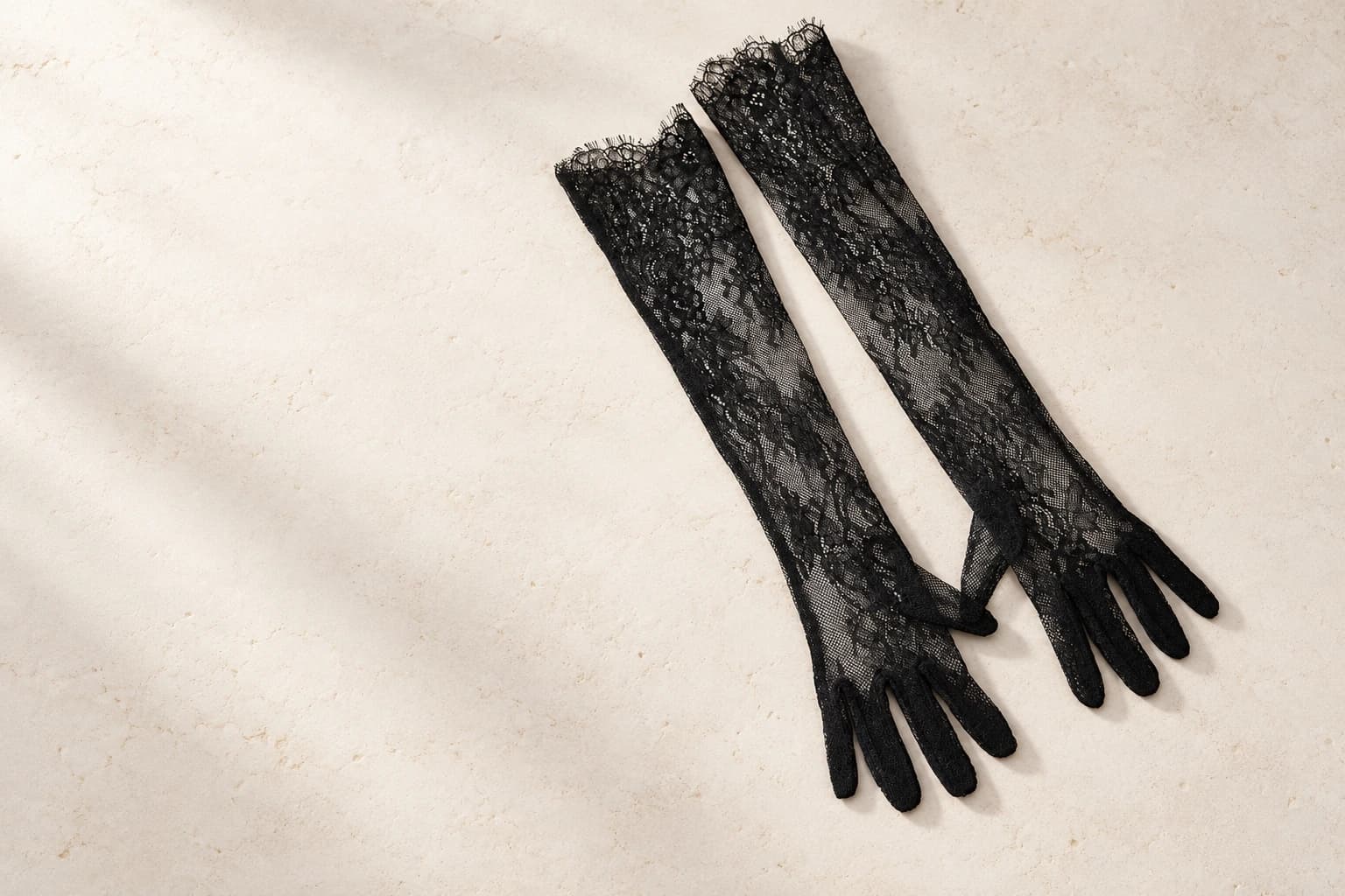 Black floral lace bridal gloves arranged on a warm ivory studio surface