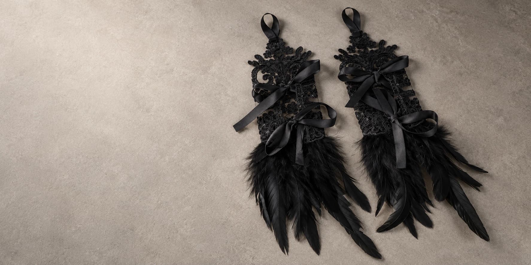 Black lace performance gloves with satin bows and feathered cuffs on a neutral studio surface